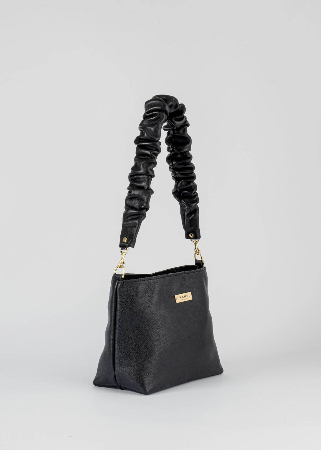 A black leather shoulder bag with a distinctive ruched strap and gold-tone hardware, shown on a light gray background.