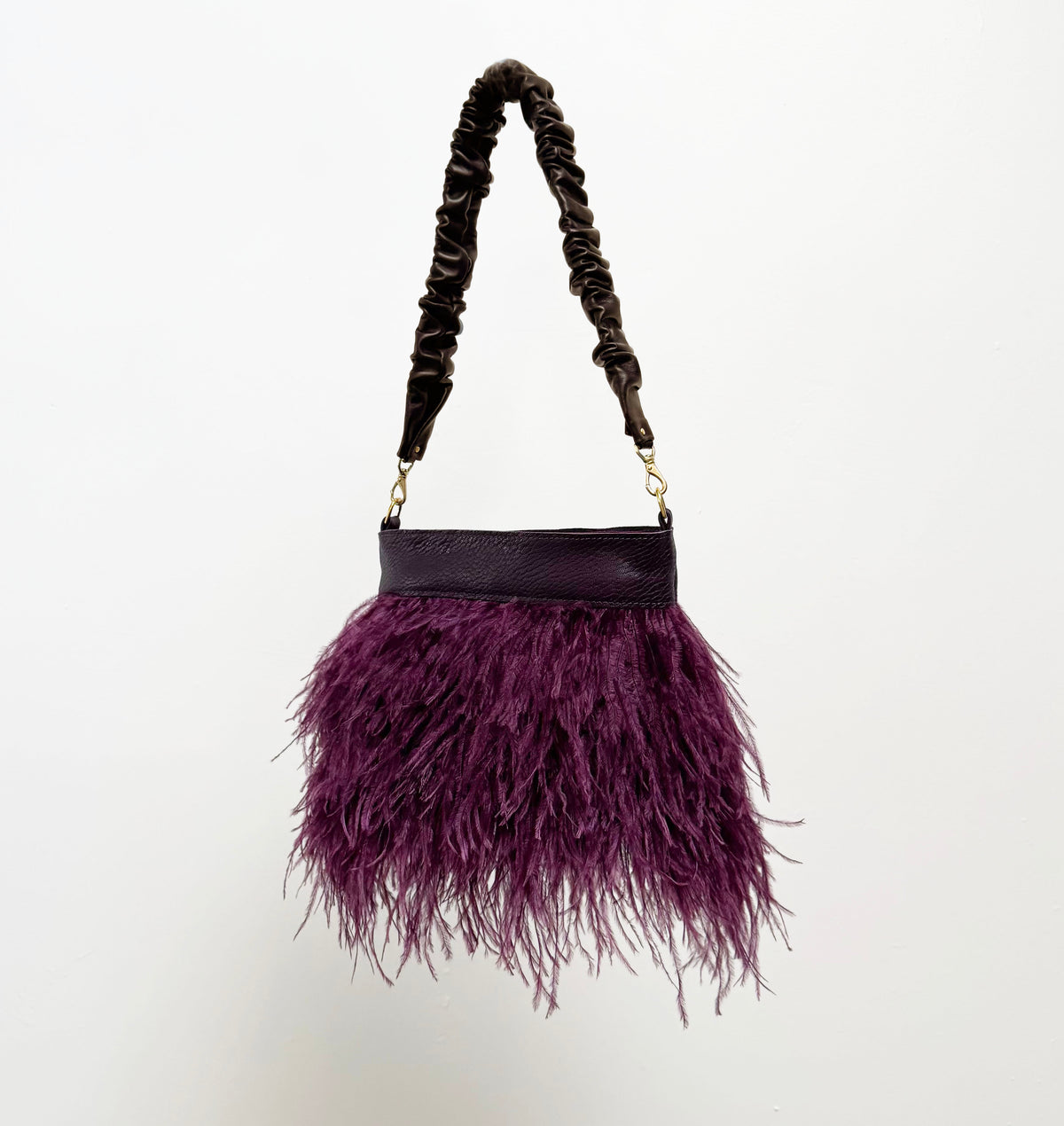 Purple feathered handbag with ruched handle on a white background